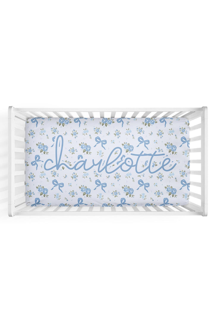 Personalized white crib sheet with blue floral and bow print, customized with the name "Charlotte" in cursive script