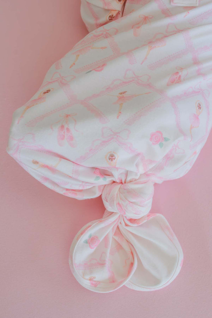 Newborn baby lying on a pink backdrop wearing a Caden Lane ballerina and roses pink print knotted gown with wooden buttons