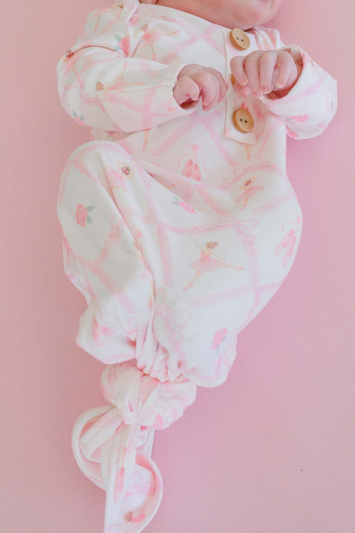 Newborn baby lying on a pink backdrop wearing a Caden Lane ballerina and roses pink print knotted gown with wooden buttons