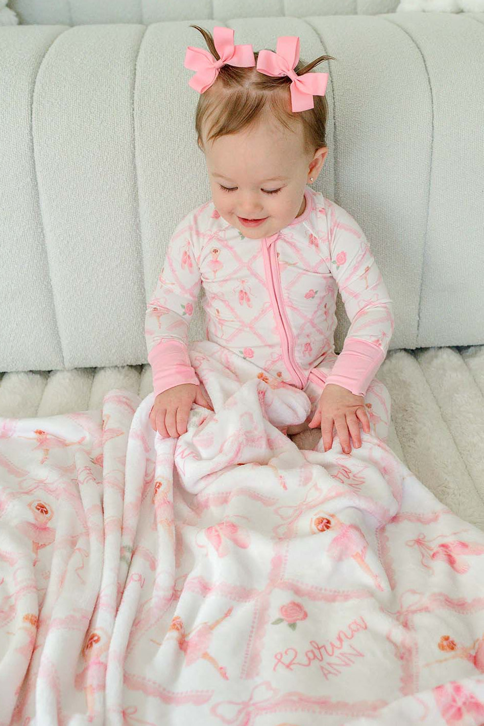 Baby girl in Caden Lane ballerina and roses pink print pajamas sitting with a matching personalized plush blanket embroidered with her name