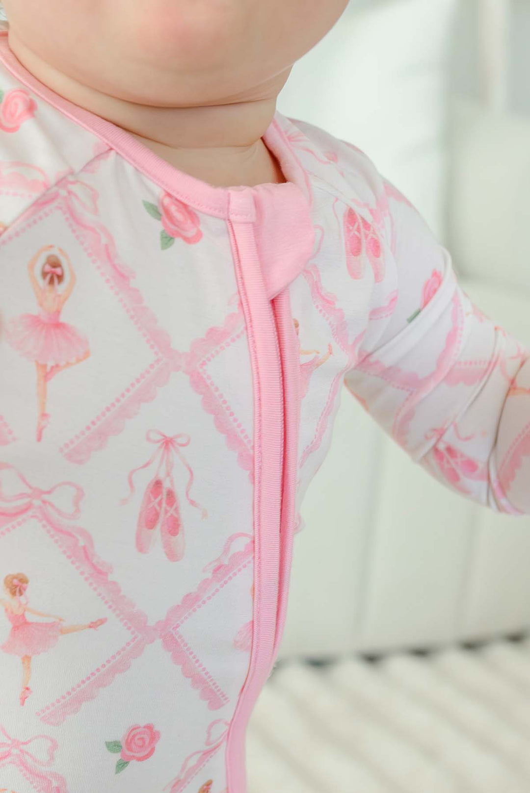 Toddler girl wearing a Caden Lane ballerina and roses pink print zip-up romper with pink cuffs
