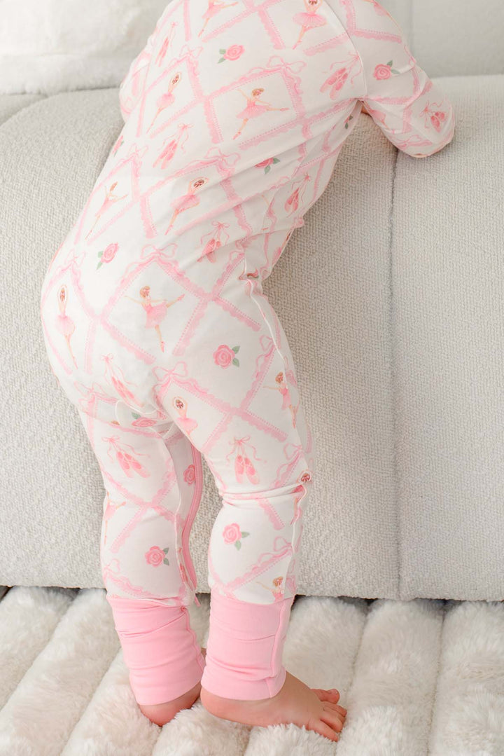 Toddler wearing a Caden Lane ballerina and roses pink print zip-up romper with pink cuffs