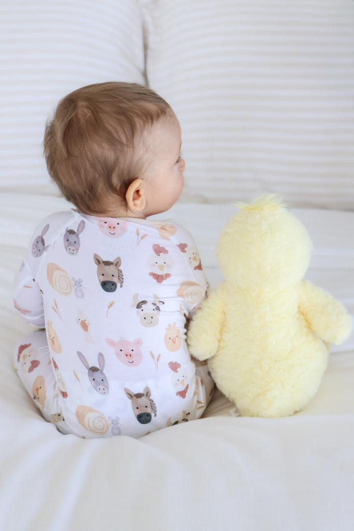 back view of boy in barnyard buddies pajama romper sitting next to a duck stuffed animal 