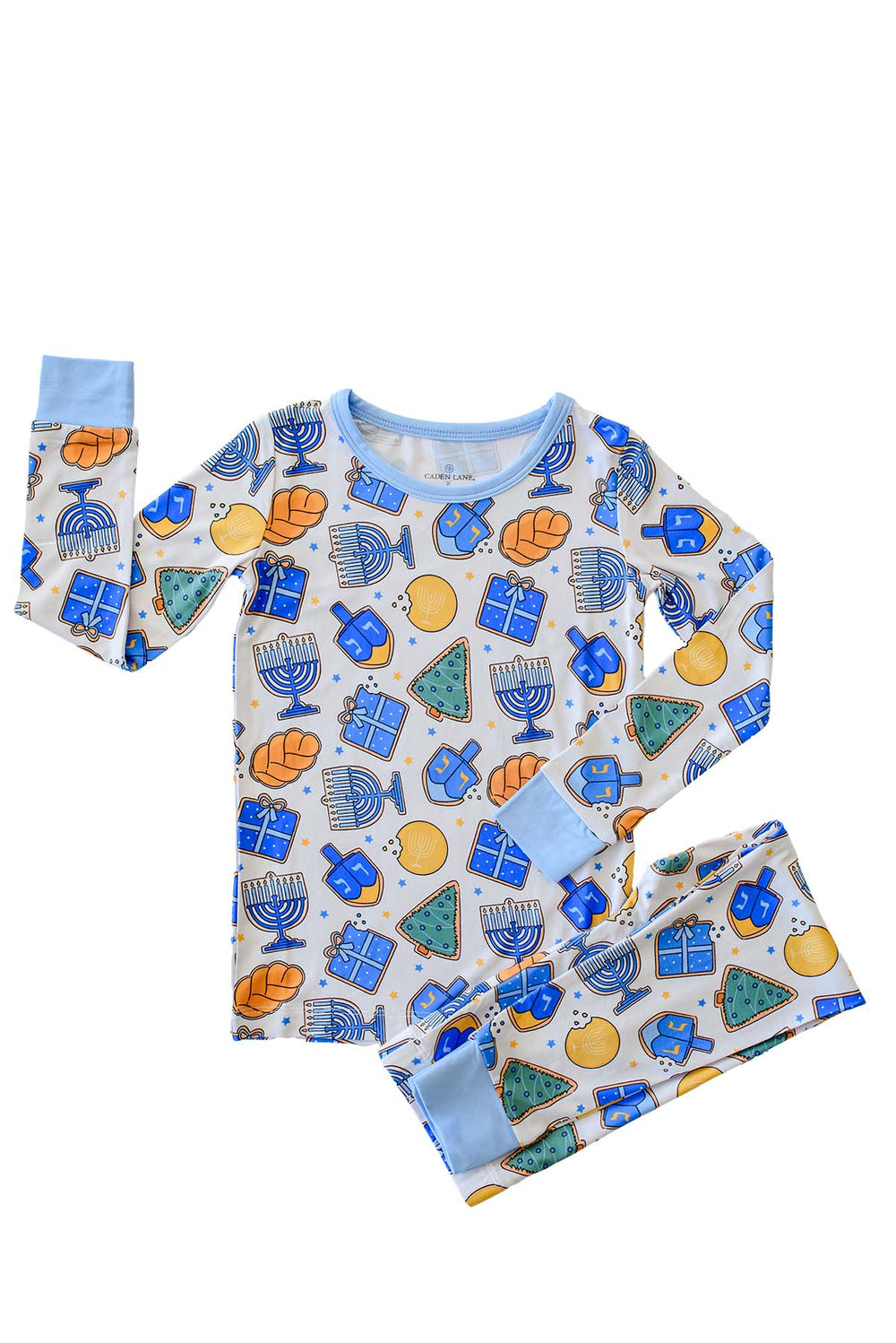 Caden Lane two-piece pajama set with blue trim, printed with Hanukkah icons like menorahs, dreidels, gifts, and Christmas trees on a cream background