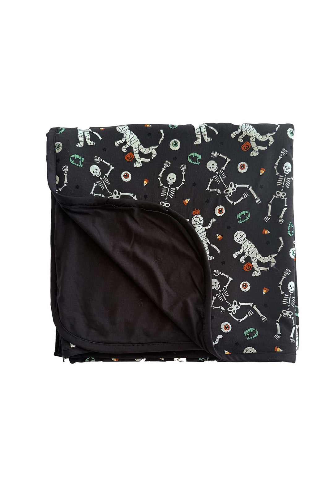 Caden Lane bamboo blanket in black, folded to show the solid black backing and a Halloween skeleton, mummy, and candy corn print, with vampire fangs and eyeball accents throughout
