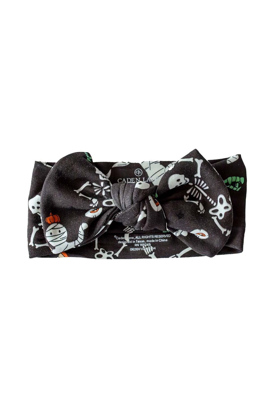 Caden Lane black knotted bow headband with a white skeleton, mummy, and candy corn Halloween print.