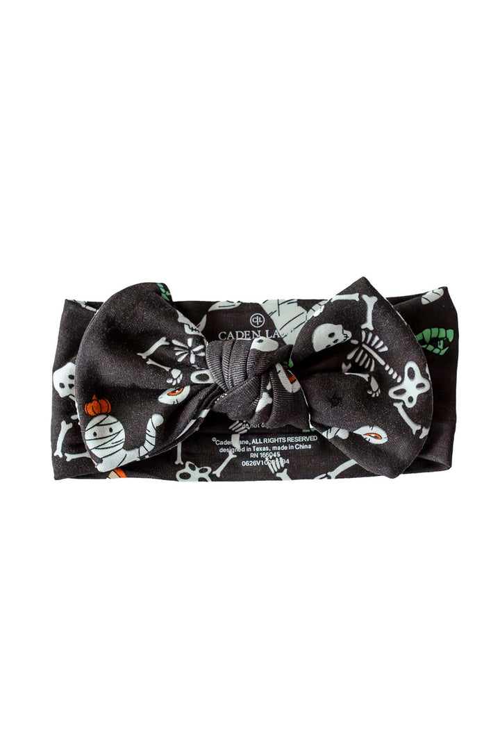 Caden Lane black knotted bow headband with a white skeleton, mummy, and candy corn Halloween print.