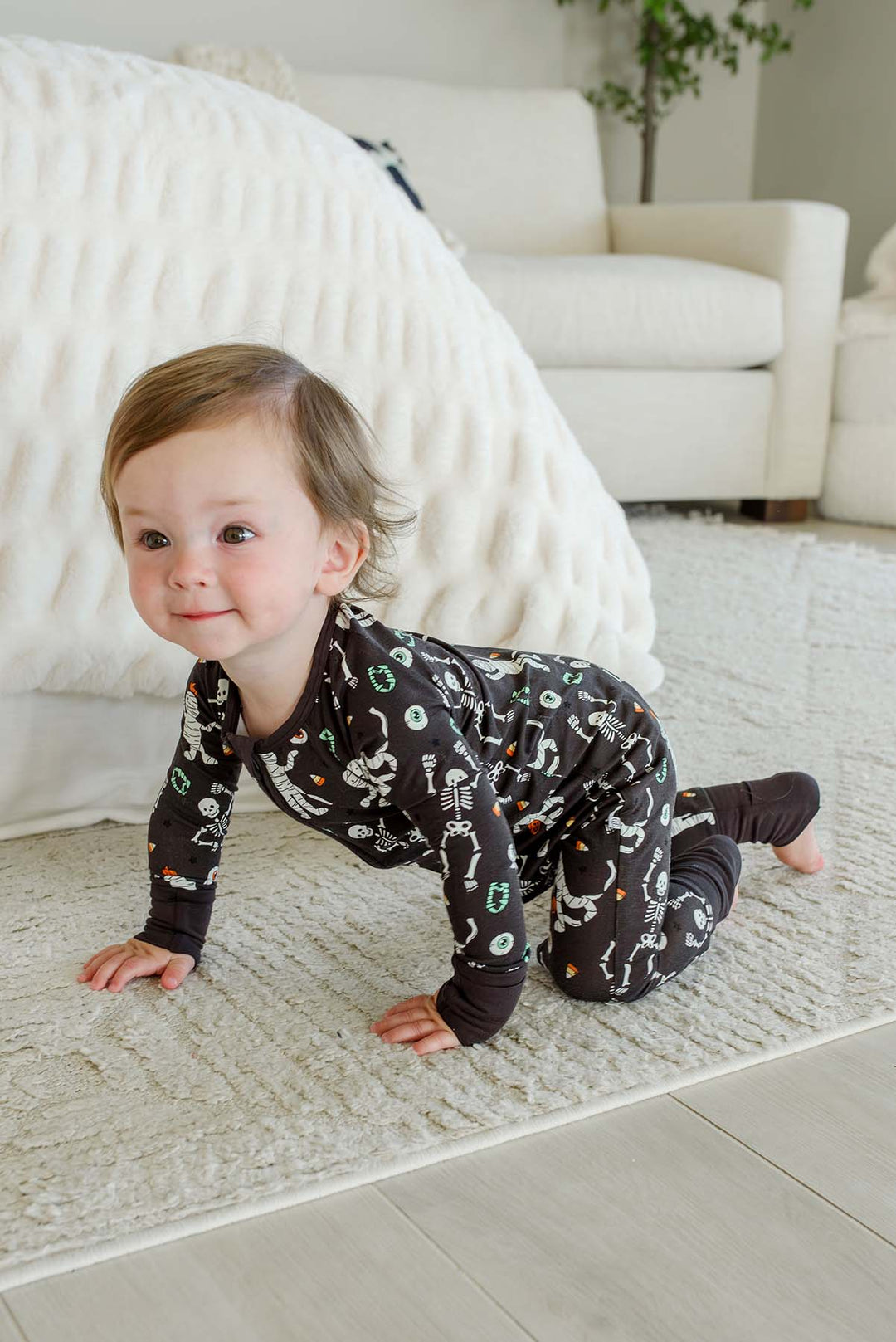 Smiling toddler crawling and wearing a Caden Lane black zip-up skeleton and mummy print romper.