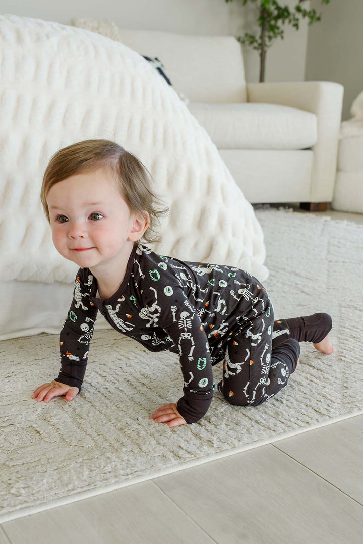 Smiling toddler crawling and wearing a Caden Lane black zip-up skeleton and mummy print romper.