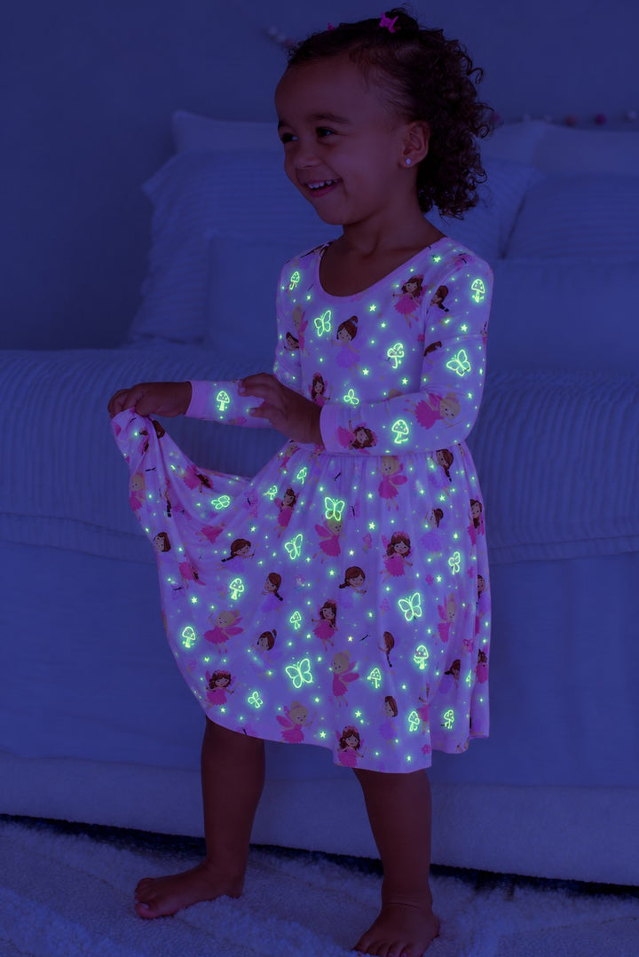 Smiling girl holding out her skirt, wearing a glowing Caden Lane pink bamboo long sleeve twirl dress in a Fairy Wishes print featuring fairies and butterflies.