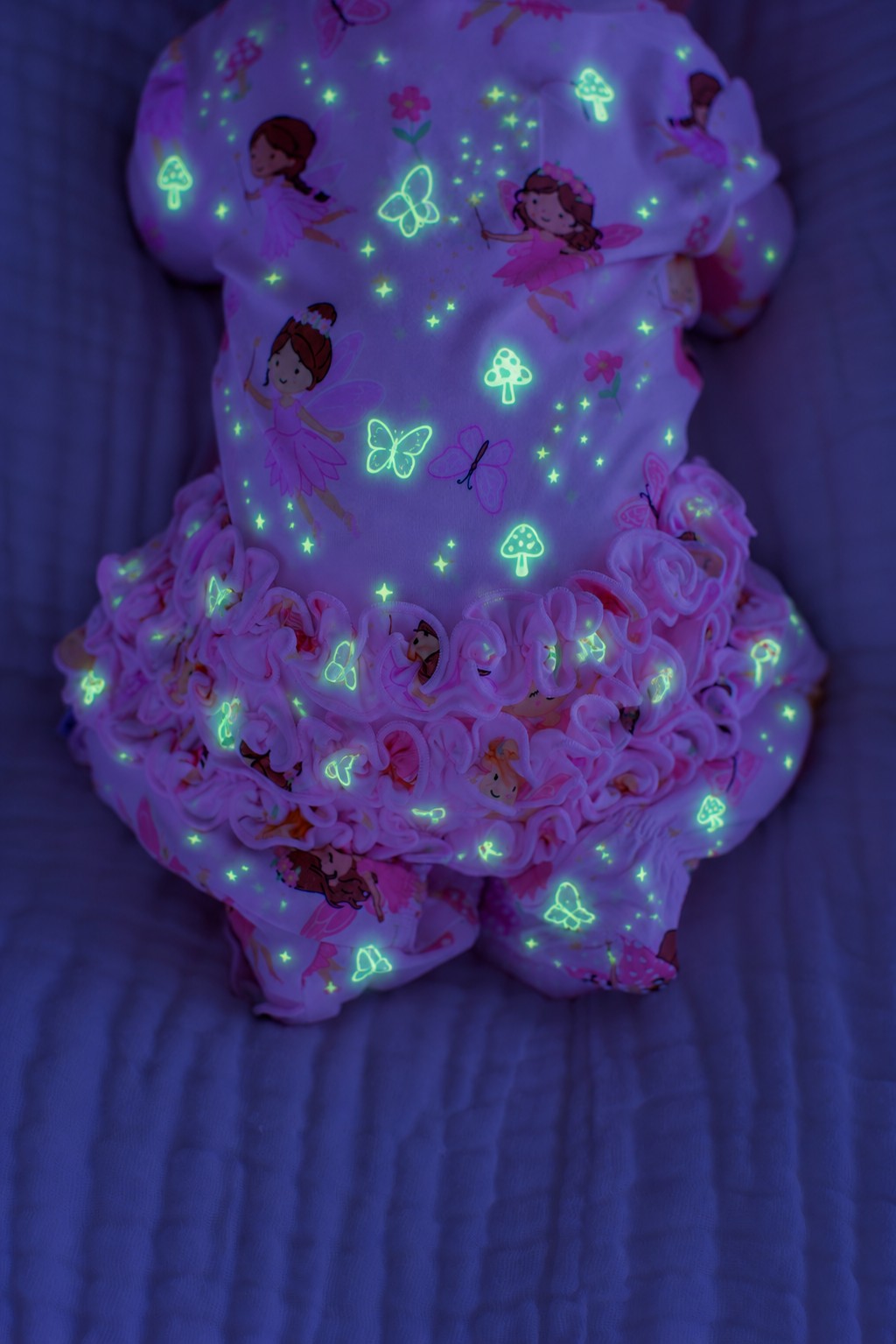Back view of a baby showing ruffled bottom tiers, wearing a glowing Caden Lane pink bamboo ruffle zipper footie in a Fairy Wishes print featuring fairies and butterflies.