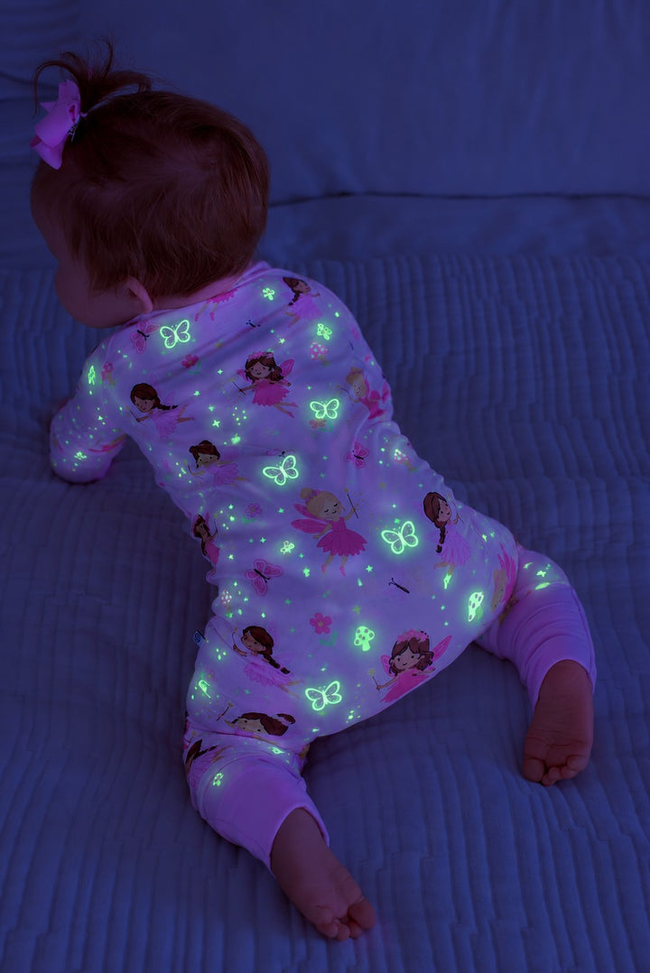 Back view of a baby crawling on a bed, wearing a glowing Caden Lane pink bamboo convertible zip romper in a Fairy Wishes print featuring fairies and butterflies.