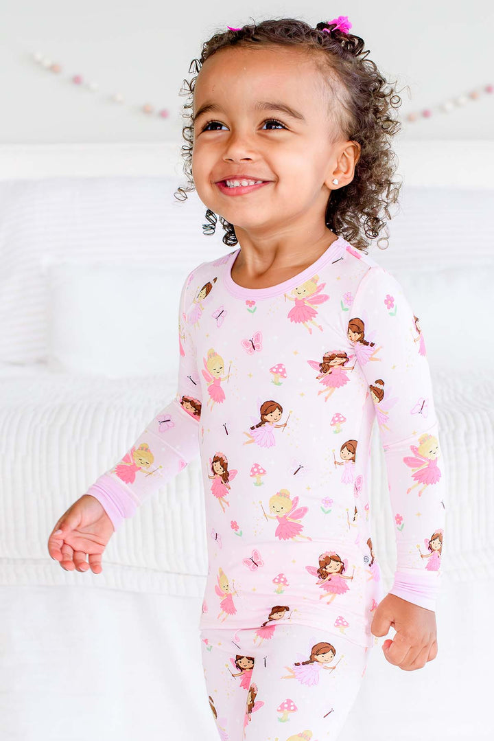 Smiling toddler girl in the light pink Fairy Wishes glow-in-the-dark two-piece bamboo pajamas with fairy print