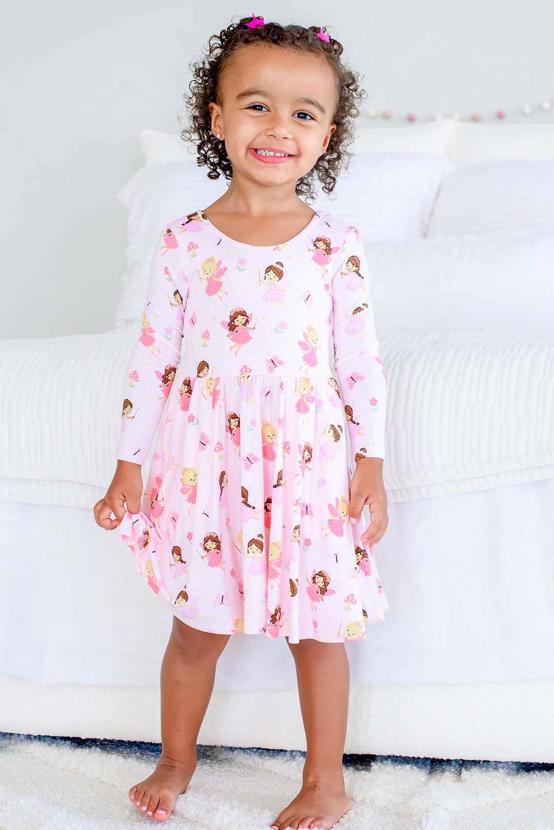 Smiling toddler girl standing in the light pink Fairy Wishes long sleeve twirl dress with fairy print