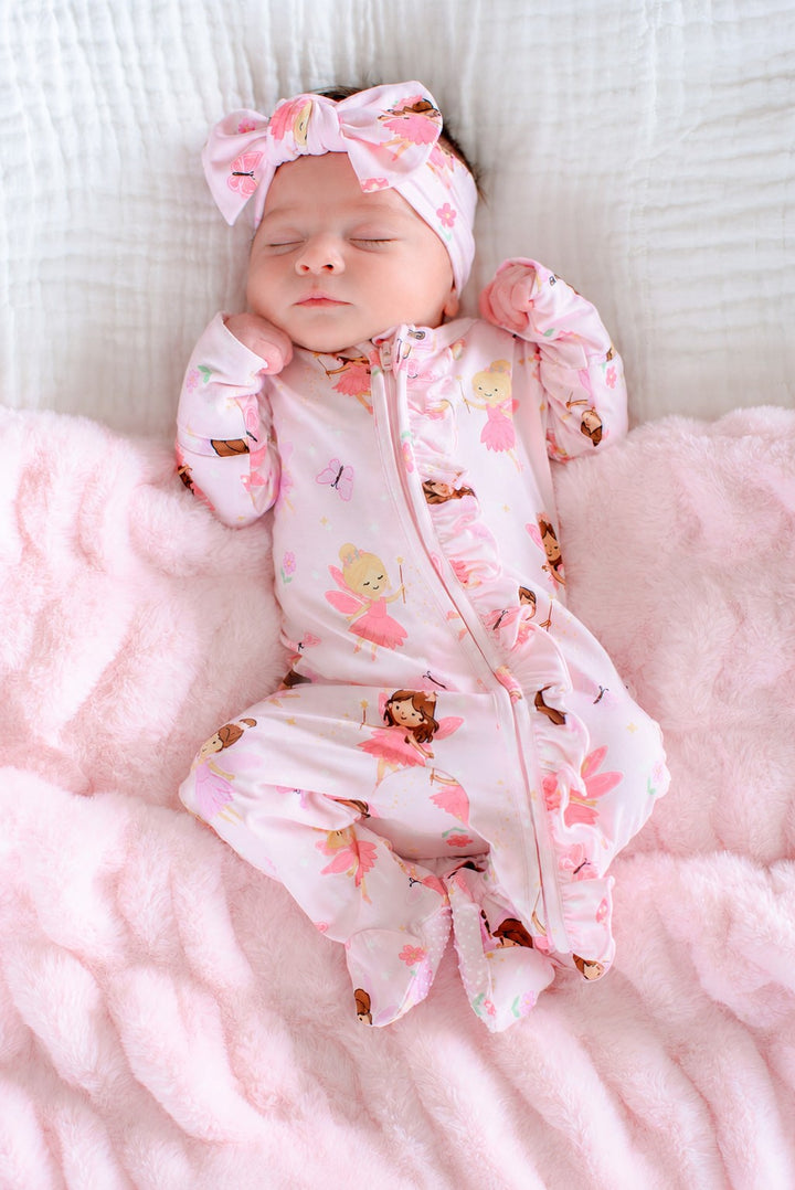 Baby lying on a pink blanket wearing the Fairy Wishes glow-in-the-dark bamboo zipper ruffle footie and matching bow headwrap