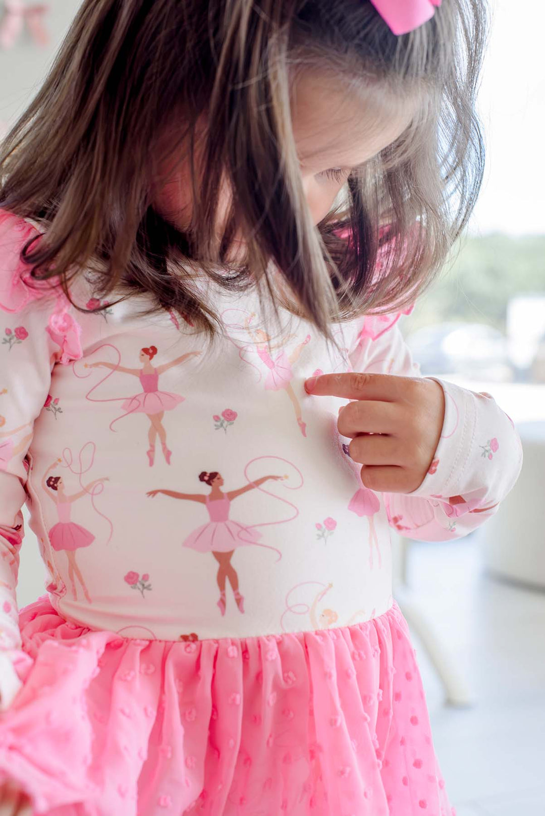 Close-up of a girl pointing to a dancer on a Caden Lane leotard in a ballerina print featuring dancers with ribbons and pink roses, with a swiss dot mesh skirt.