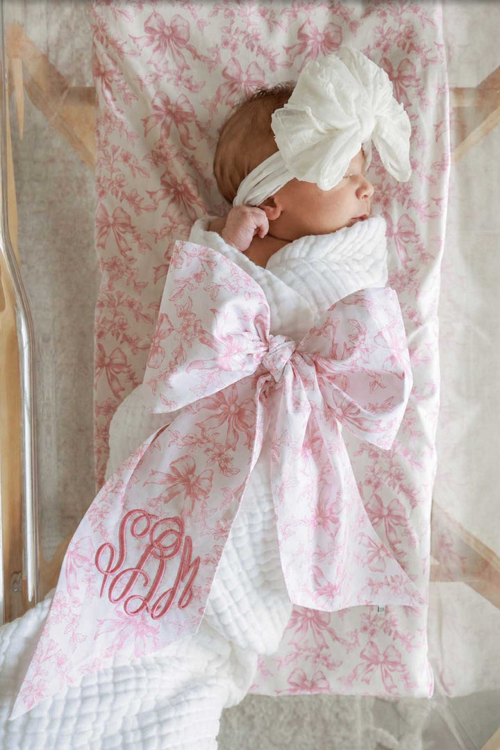 baby girl laying in bassinet wrapped in fancy frills bow sash with white fluffy bow