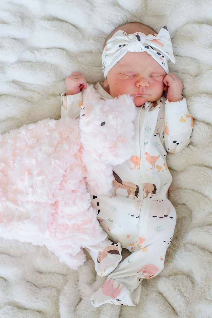 Sleeping newborn in Caden Lane farm animal footie pajamas and matching knotted headband, holding a pink faux fur lovey