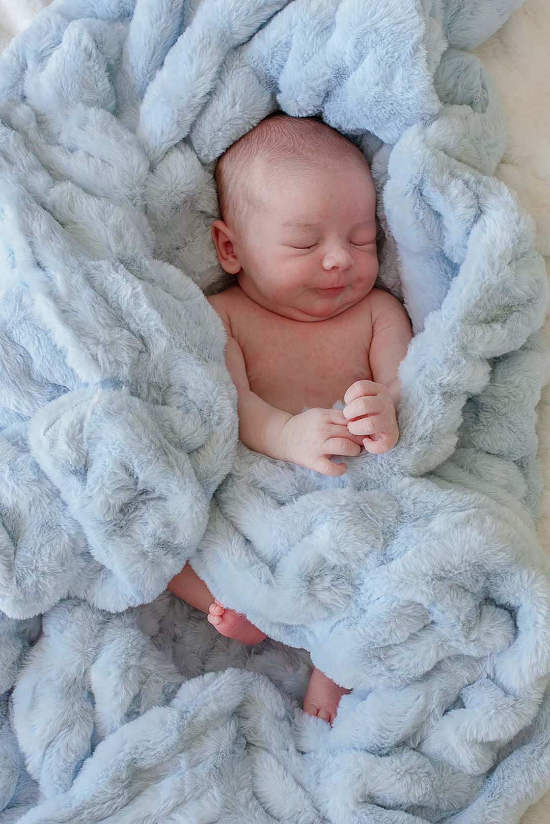 Newborn baby lying content and swaddled in an ice blue double-ruched faux fur blanket
