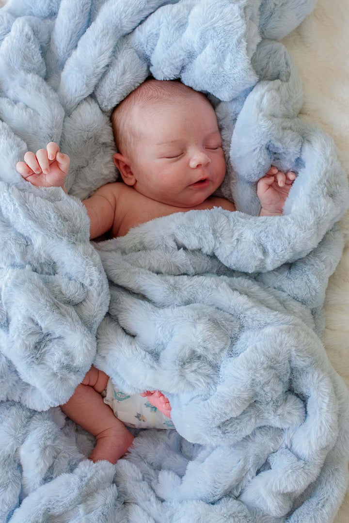 Newborn baby resting calmly in an ice blue double-ruched faux fur blanket