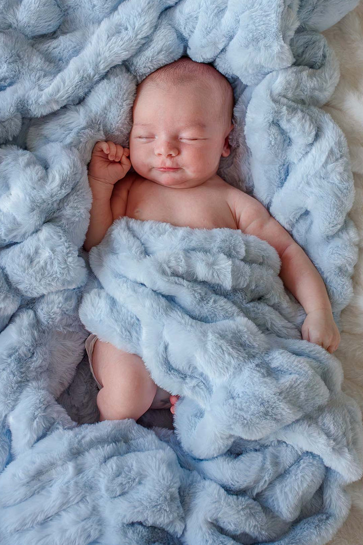 Sleeping newborn baby wrapped in an ice blue double-ruched faux fur blanket