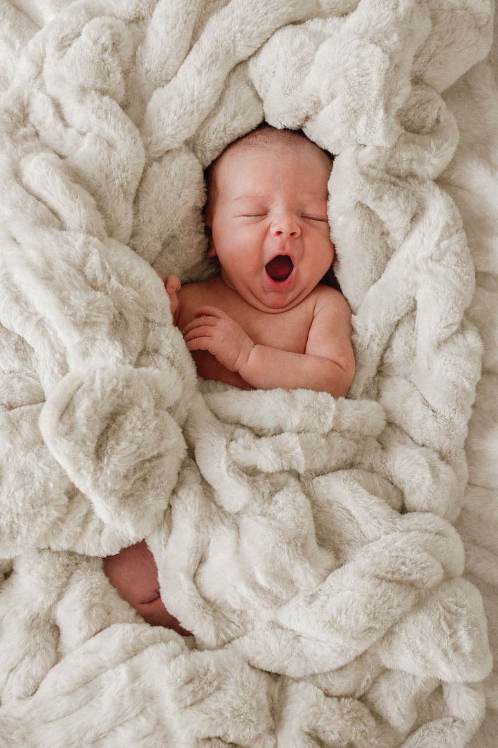 Newborn baby yawning while wrapped in a sand-colored double-ruched faux fur blanket