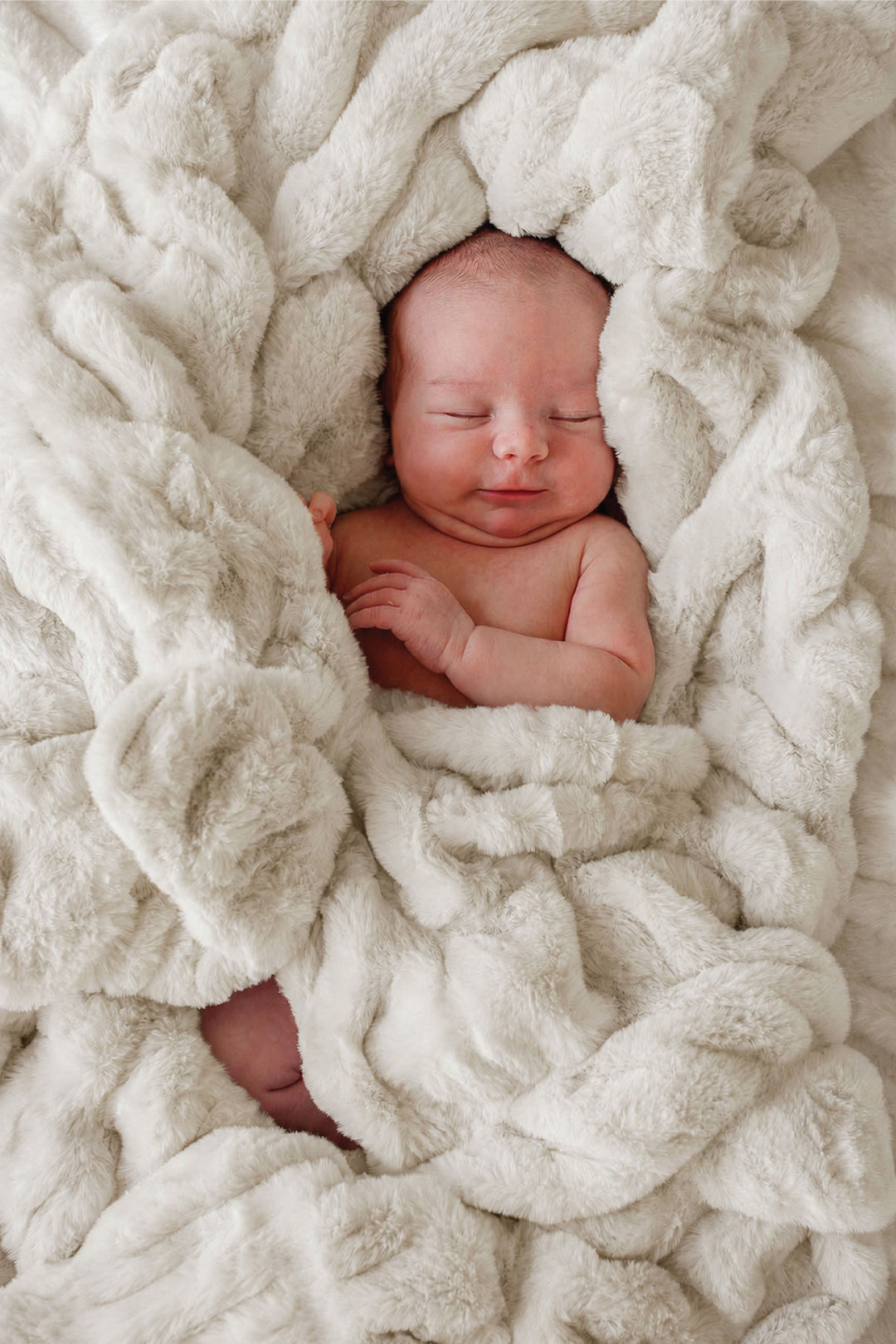 Sleeping newborn baby swaddled in a sand-colored double-ruched faux fur blanket