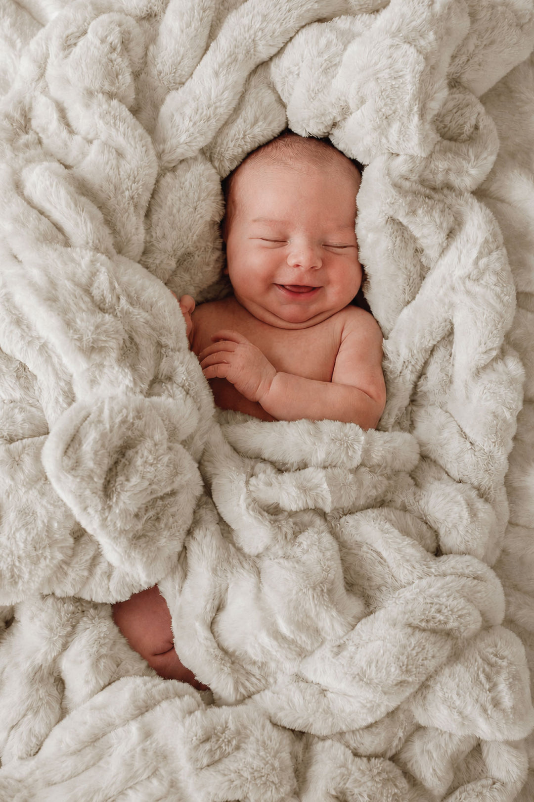 Smiling newborn baby swaddled in a sand-colored double-ruched faux fur blanket