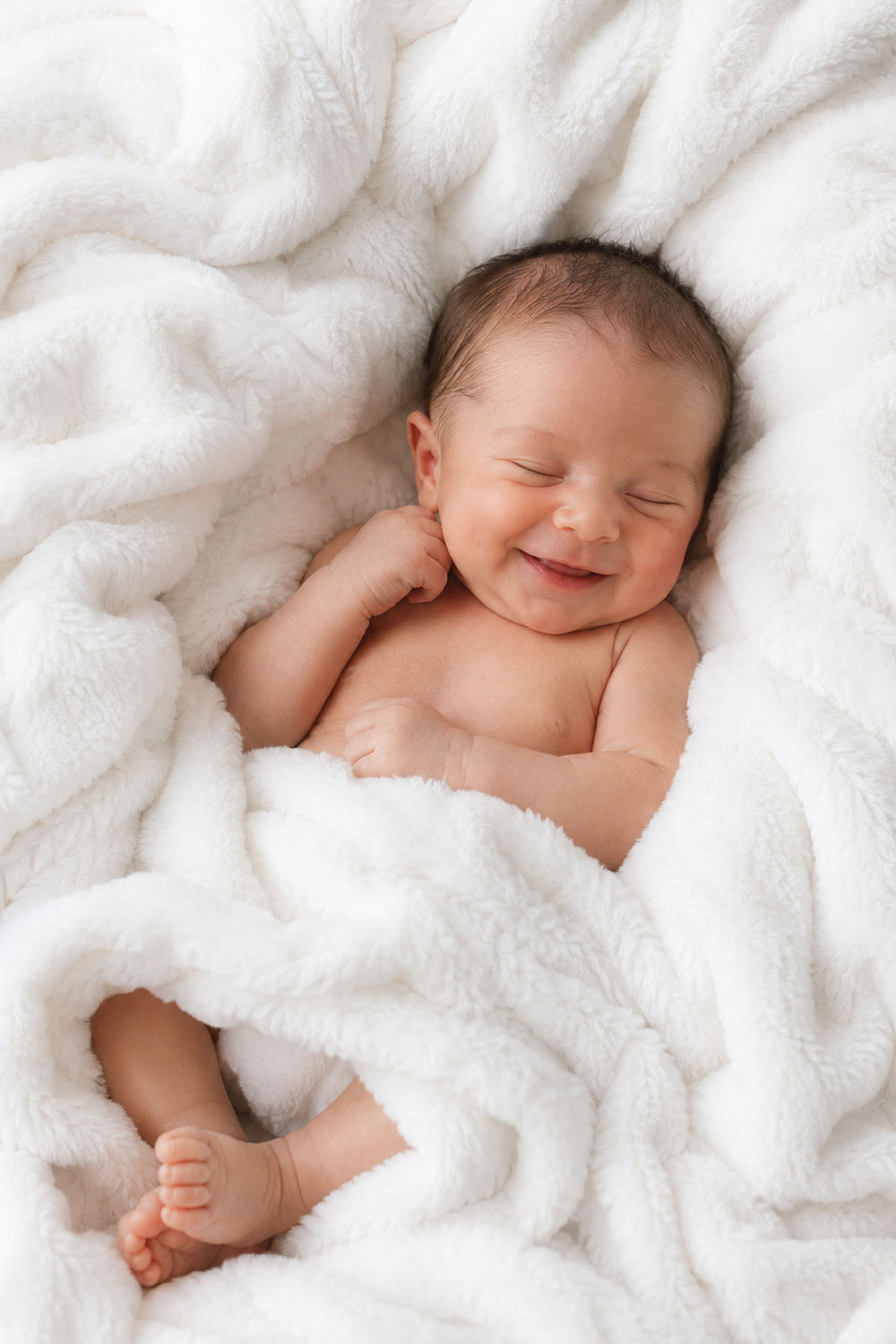 Smiling newborn baby lying on a winter white double-ruched faux fur blanket