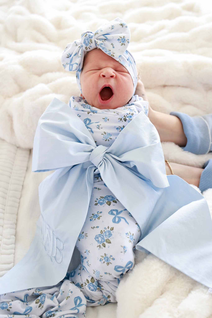 Yawning baby wearing a Tied In Blooms bow headwrap and outfit in blue floral and bow print, wrapped with a large light blue ribbon bow