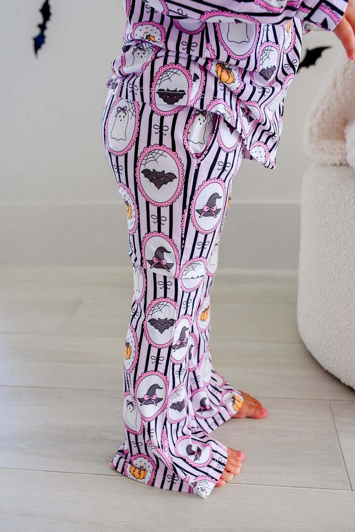 Young girl wearing a Caden Lane pink and black striped button-up two-piece flare pajama set with ghost, bat, and pumpkin cameo print