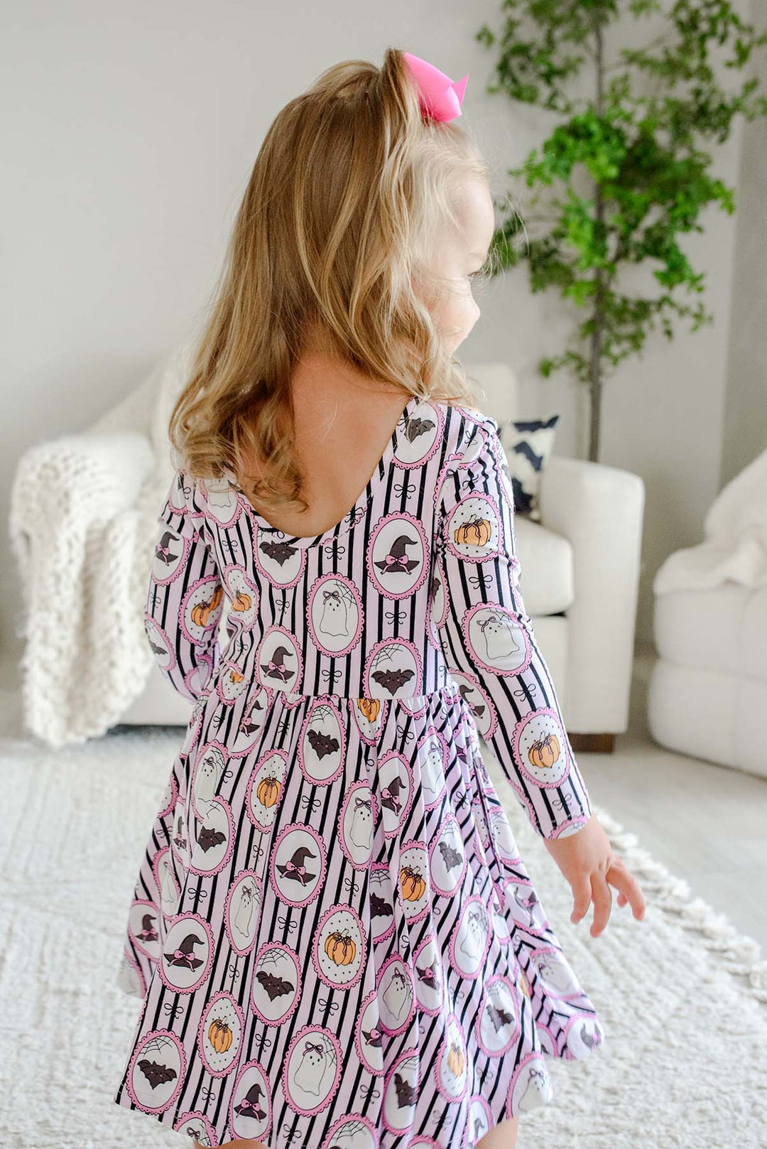 Back view of a young girl twirling in a purple and white striped Halloween-print dress with pumpkin, bat, ghost, and witch hat designs.