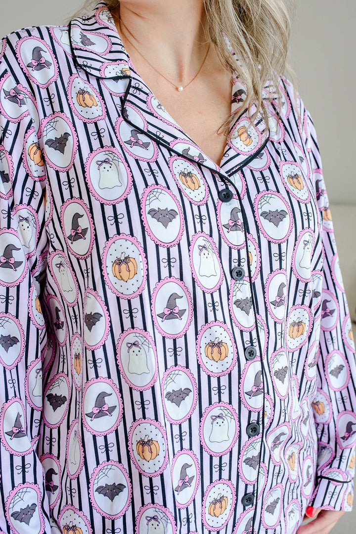 A woman wearing a long-sleeve pajama shirt with a Halloween-themed print of ghosts, pumpkins, and witch hats on a black and white striped background.