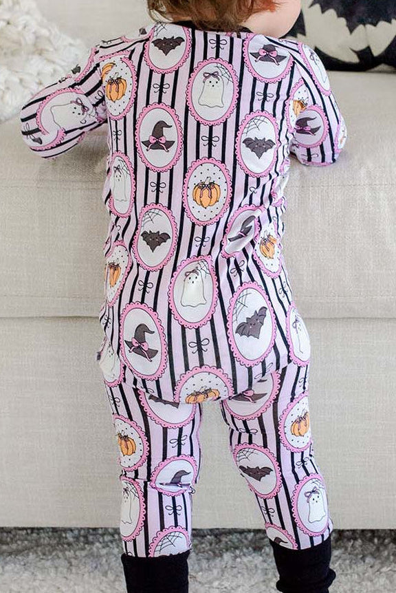 Back view of a toddler standing barefoot, wearing a Caden Lane pink and black striped Halloween romper with ghost, bat, pumpkin, and witch hat cameo print and black cuffs.