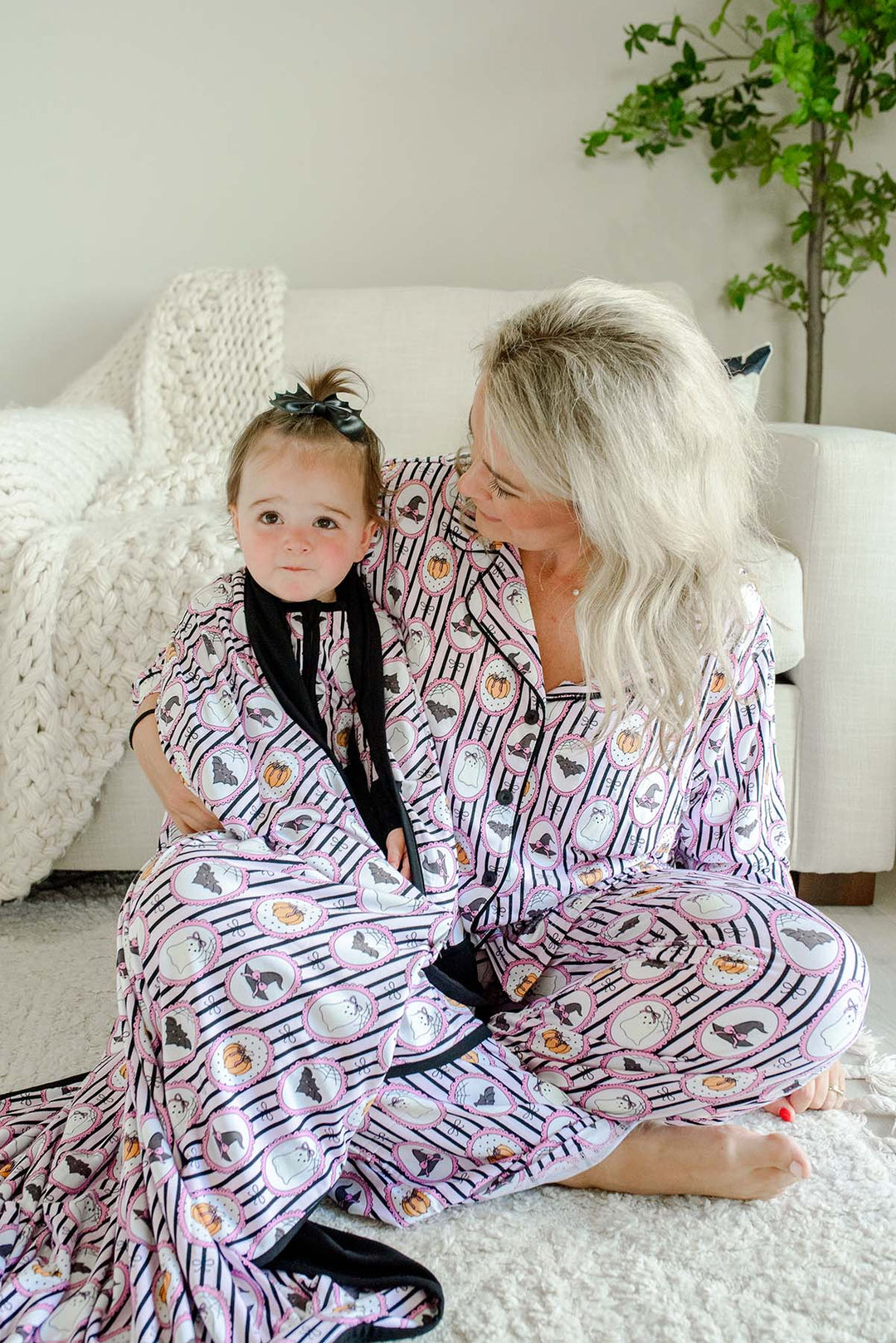 Mom and baby in a Caden Lane pink and black striped bamboo ghost, bat, pumpkin, and witch hat cameo print, with matching blanket wrapped around baby