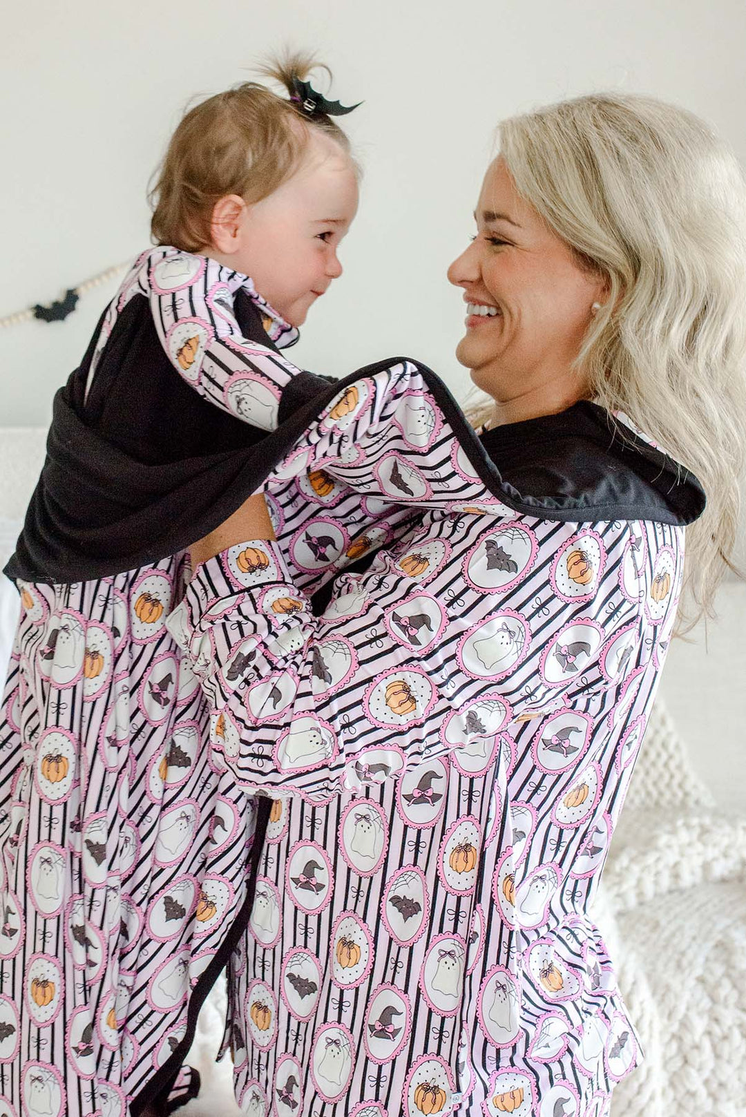 Mom and baby in a Caden Lane pink and black striped bamboo ghost, bat, pumpkin, and witch hat cameo print, with matching blanket wrapped around baby