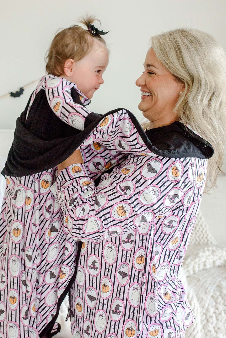 Mom and baby in a Caden Lane pink and black striped bamboo ghost, bat, pumpkin, and witch hat cameo print, with matching blanket wrapped around baby