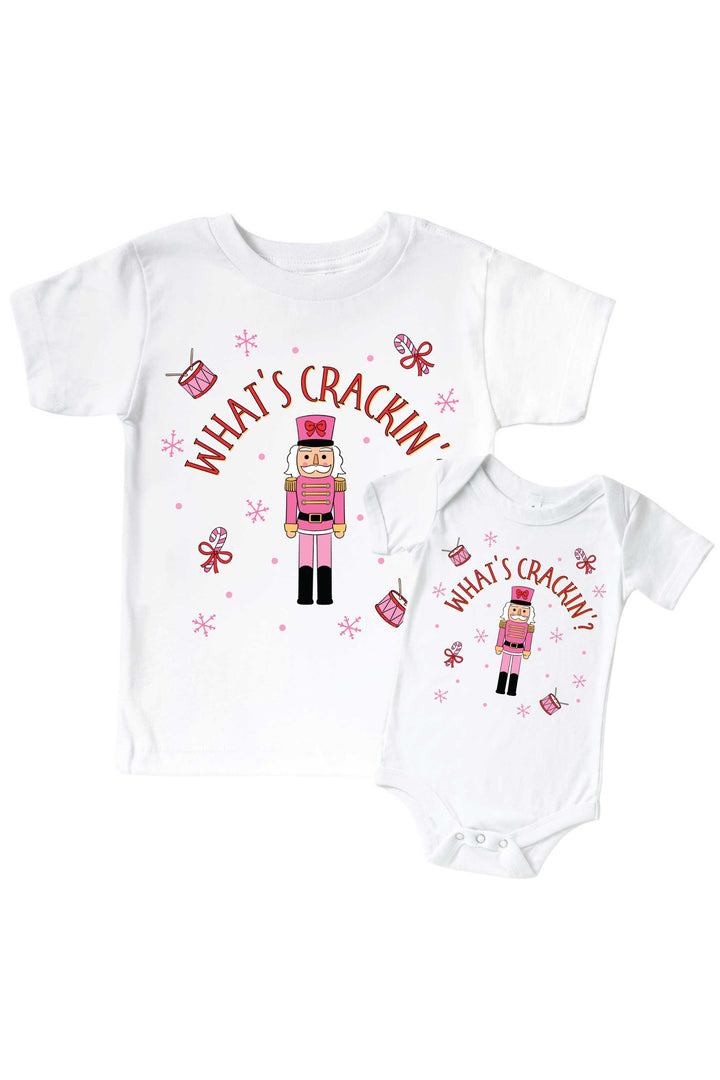 Caden Lane's matching "What's Crackin'" t-shirt and onesie featuring a pink toy soldier nutcracker with snowflakes, candy canes, and drums, laid flat together for a sibling set.