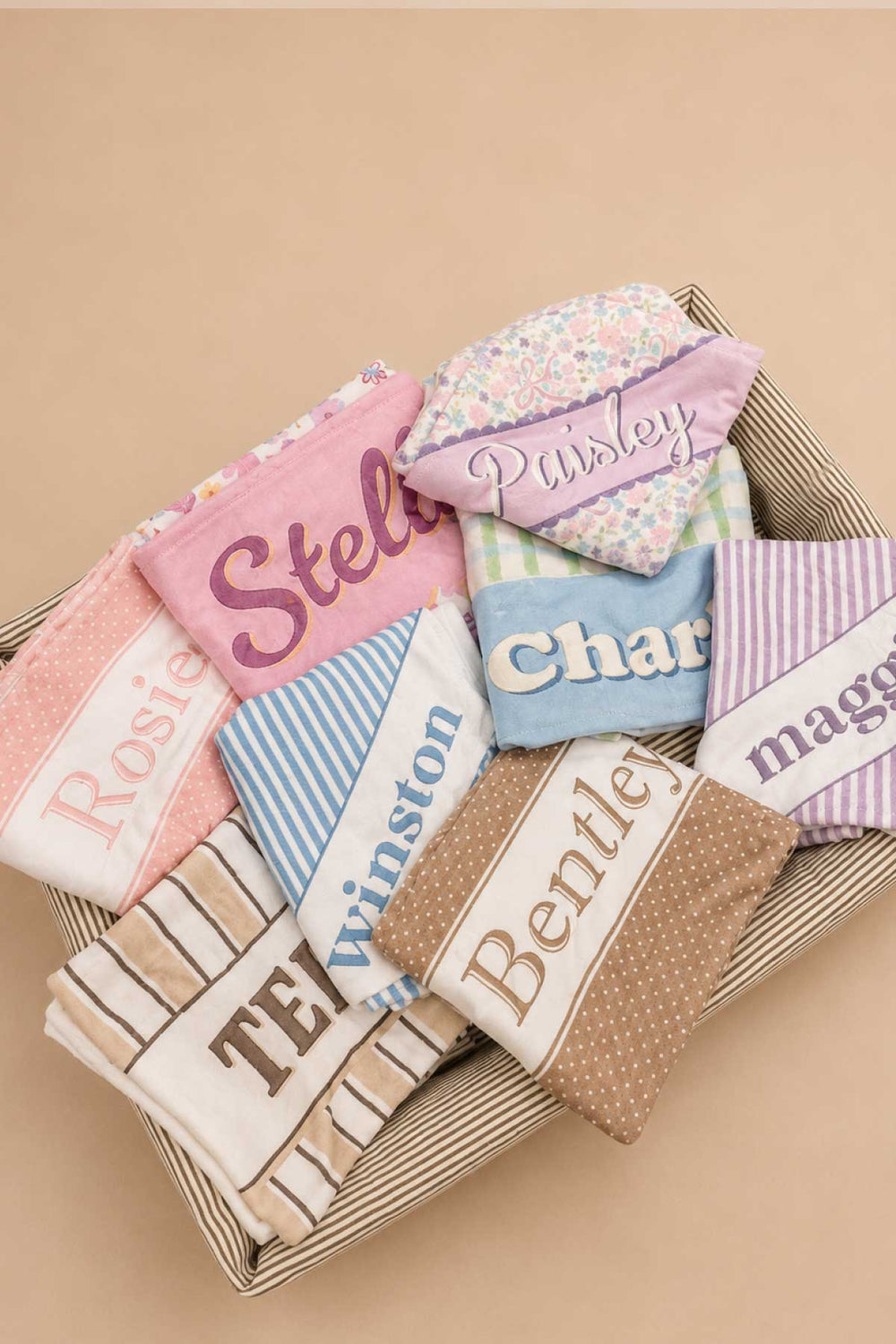 A basket filled with multiple personalized pet blankets in various prints and colors, including the Ribbon Garden print (labeled "Paisley"), showcasing the full range of customization options available