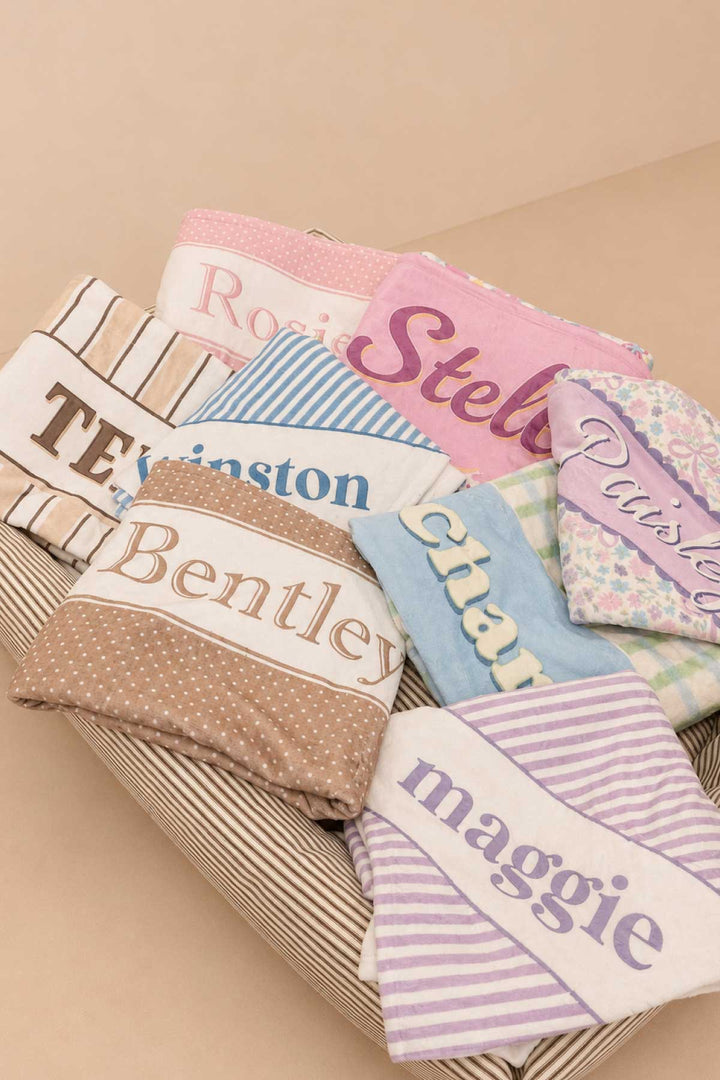 Collection of personalized pet blankets stacked together in various prints and colors, each with a unique pet name showing customization options