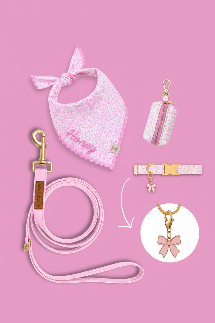 Pink floral pet accessories flatlay on pink background with bandana, poop bag holder, leash, and collar, featuring a pink bow charm highlighted in a circle callout