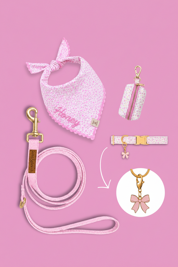 Pink floral pet accessories flatlay on pink background with bandana, poop bag holder, leash, and collar, featuring a pink bow charm highlighted in a circle callout