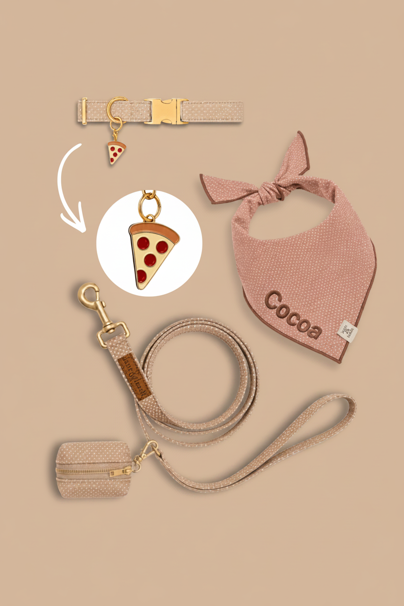 Neutral tan pet accessories flatlay on tan background with collar, bandana, leash, and poop bag holder, featuring a pizza slice charm highlighted in a circle callout