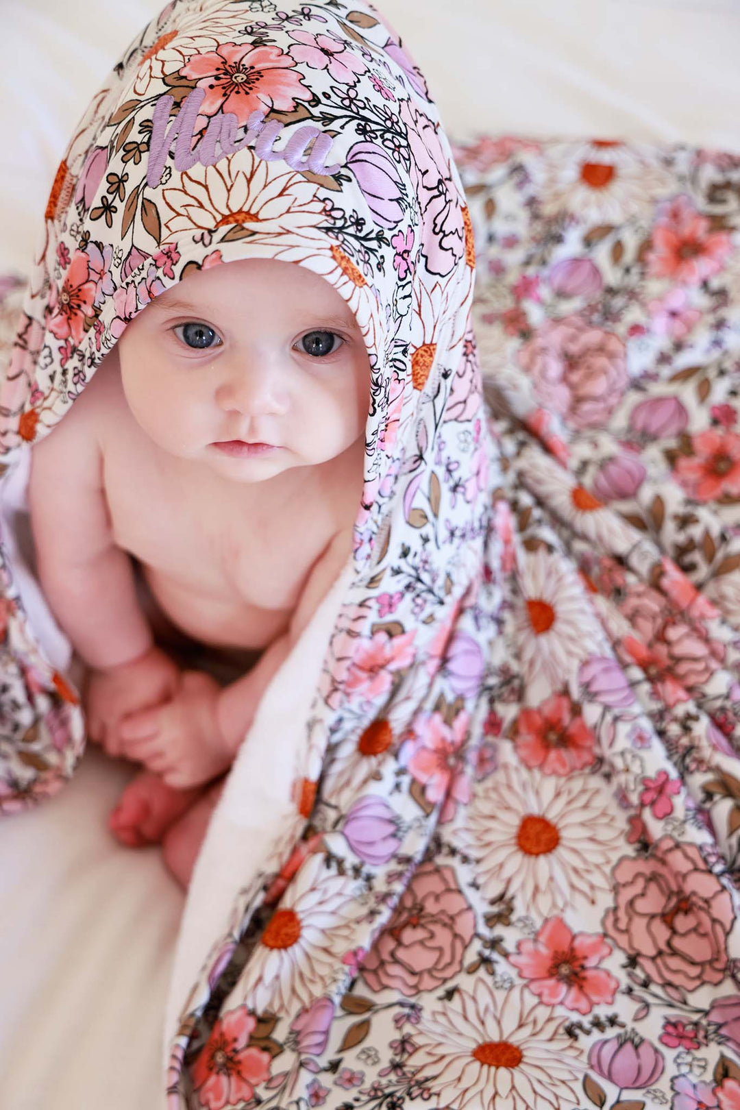 baby with pink and purple floral embroidered hooded towel on head