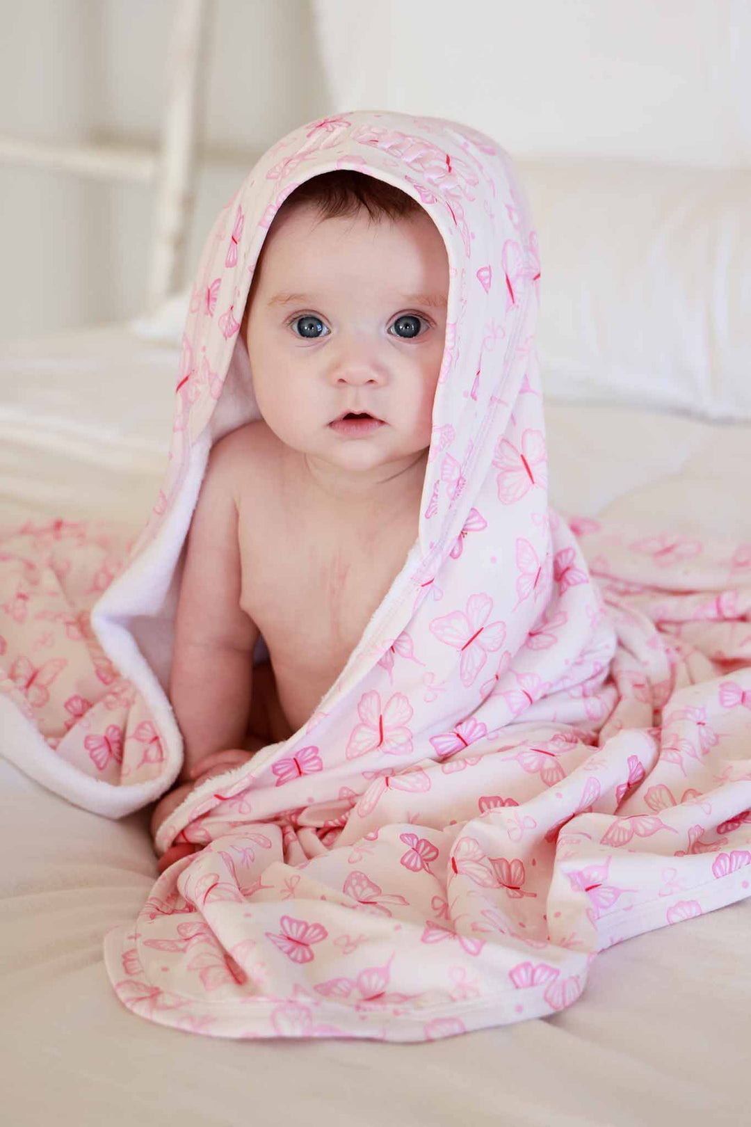 Embroidered Bamboo Hooded Towel in Blooming Butterflies print - baby sitting upright peeking out from under the pink butterfly-print bamboo towel draped over them