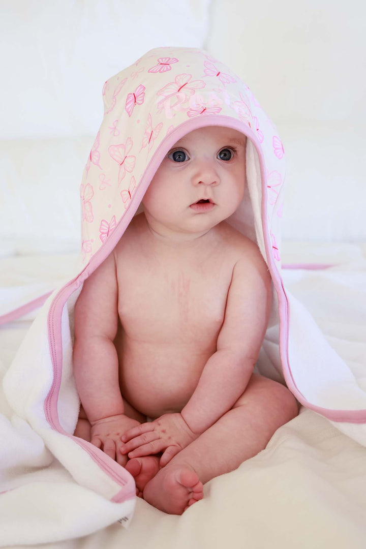 Embroidered Bamboo Hooded Towel in Blooming Butterflies print - baby sitting upright with pink butterfly-print bamboo towel worn as a hooded cape, showing the full towel drape