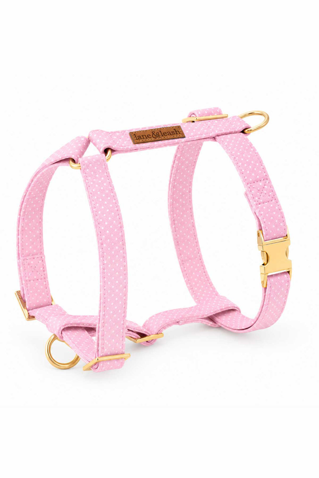 Pink polka dot H-style strap dog harness with gold hardware buckles and D-ring attachment points on a white background