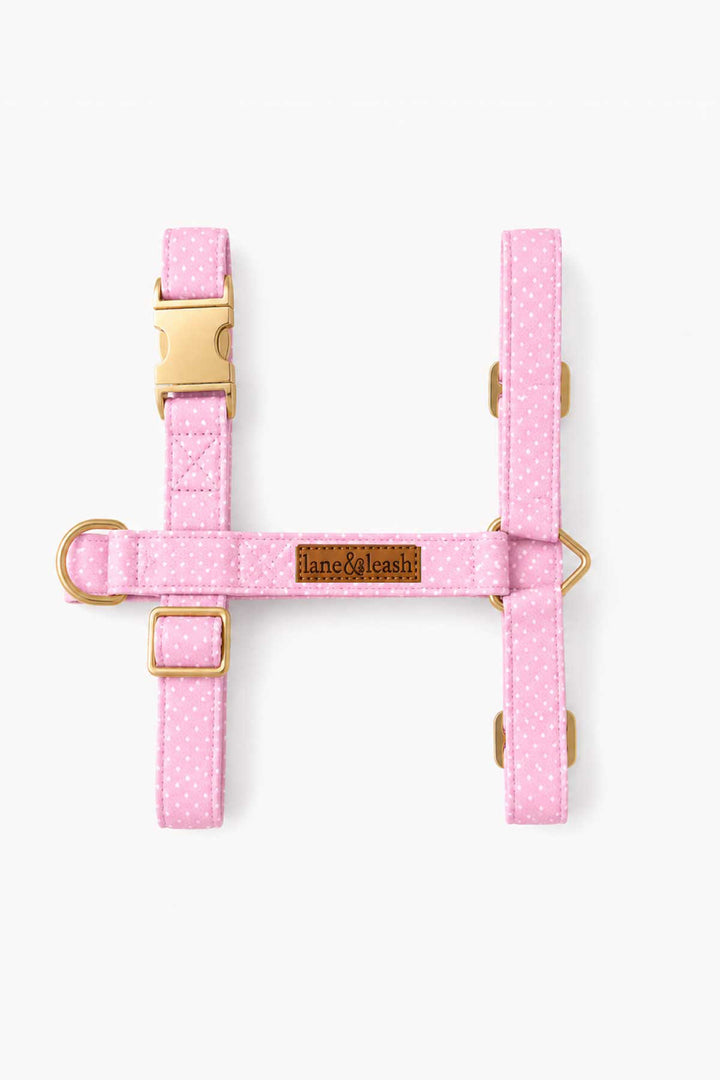 Flat lay top view of pink polka dot H-style dog harness showing the H-shape layout with gold buckle and D-ring hardware