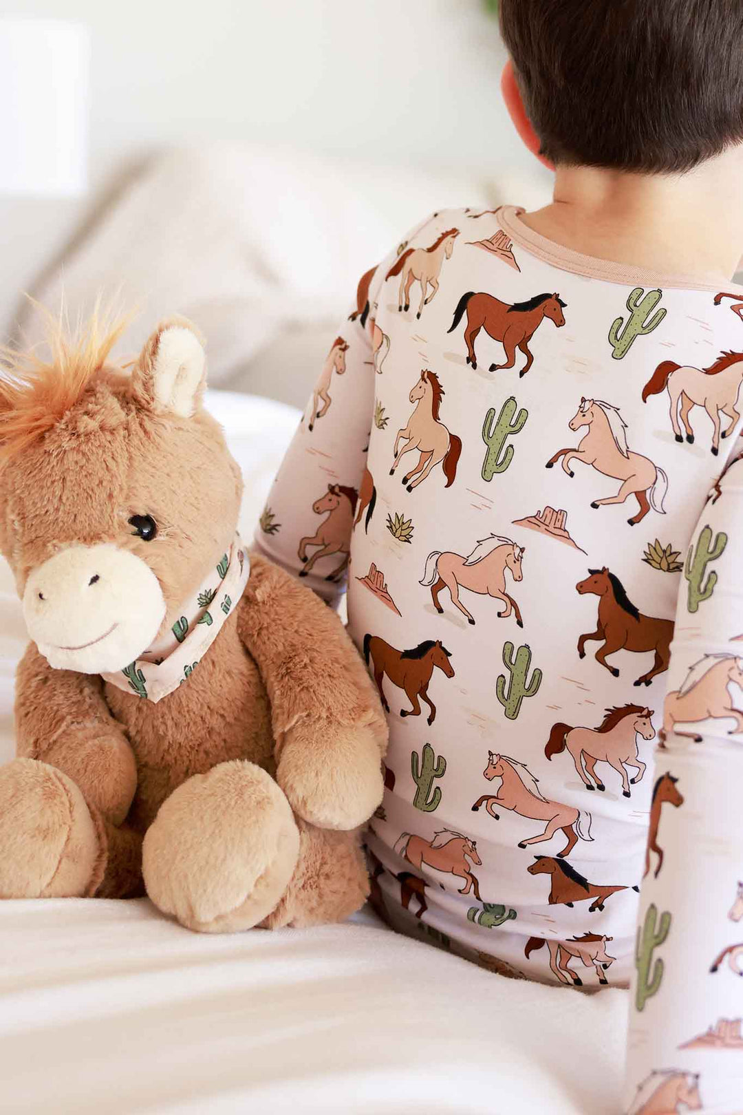 boy in horse and cactus pajamas sitting next to a horse stuffed animal