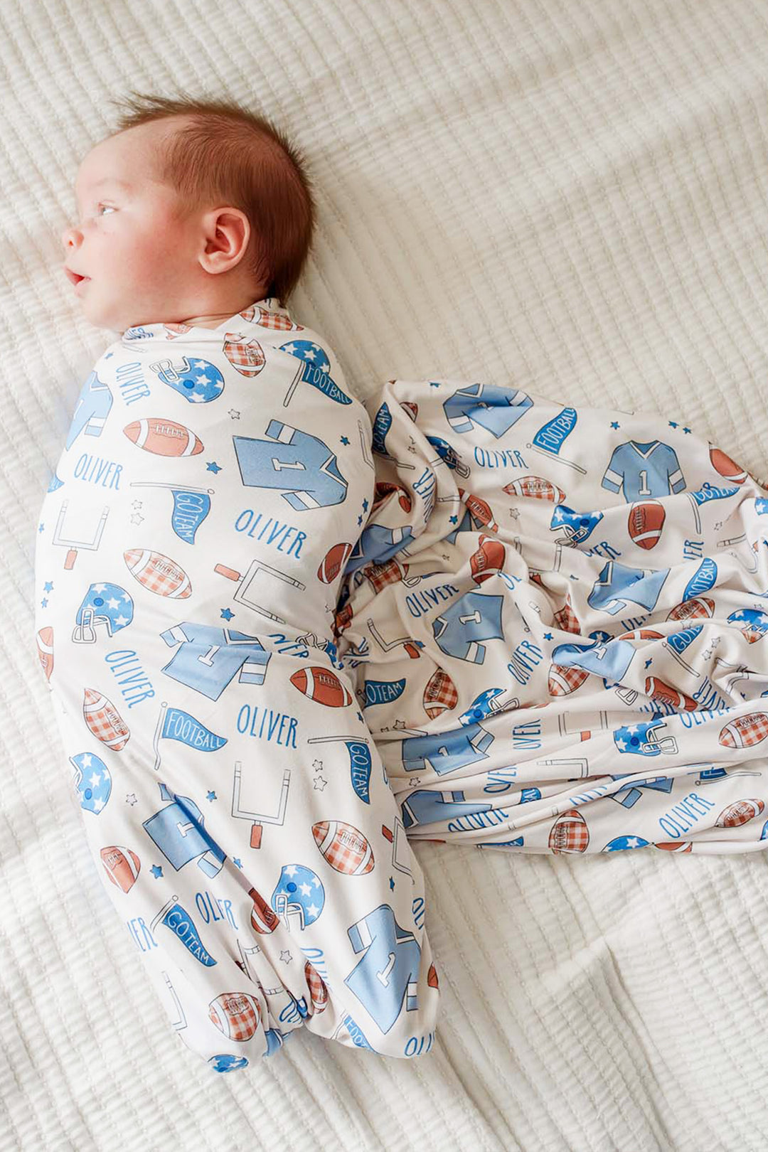 baby wrapped in a Caden Lane huddles and cuddles blue football swaddle. 